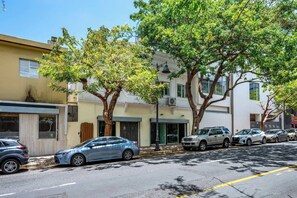 Une rue bordée de voitures garées et d’arbres, des bâtiments aux styles architecturaux variés et un ciel dégagé.