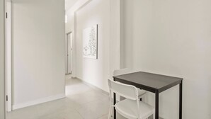 A minimalist room with a dark wooden table and white chairs, a white door, and a wall-mounted artwork. - Barrio Sanctuary - Sol (San Juan city)