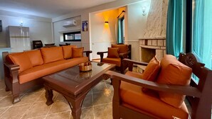 Ein Wohnzimmer mit Sofa, Sesseln, einem Couchtisch, einem Kamin und einer Küchenzeile inklusive Kühlschrank.