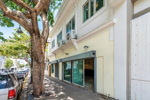 Un bâtiment doté de grandes fenêtres, avec un arbre devant et des voitures garées le long de la rue.