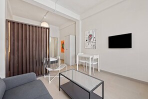 A modern living room with a glass coffee table, white chairs, a grey sofa, a wooden slatted door, and a white wall with a black framed artwork. - Barrio Sanctuary - Encanto (San Juan city)