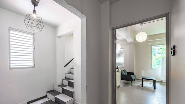 Eine Treppe mit schwarz-weißen Fliesen, eine geometrische Pendelleuchte und Blick in einen Raum mit einer Couch und einem Tisch.