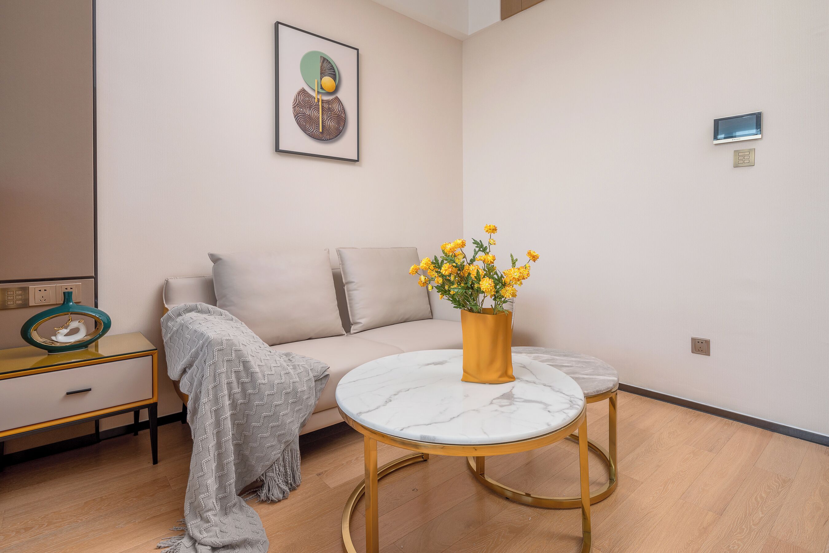 A modern living room with a sofa, a round marble table, a vase with flowers, and a wall-mounted artwork.