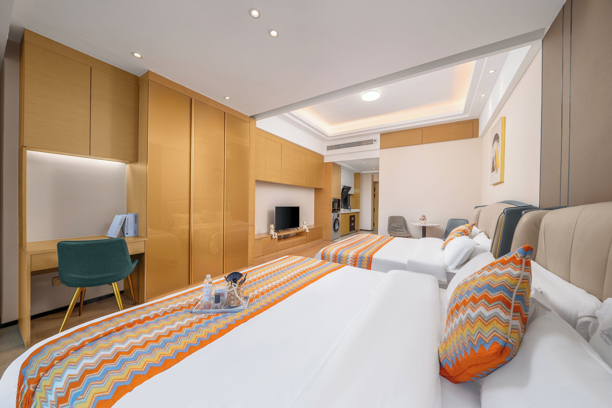 Ein Hotelzimmer mit zwei Betten, einem Schreibtisch, einem Sessel, einem Fernseher und einem kleinen Tisch mit einer Lampe.