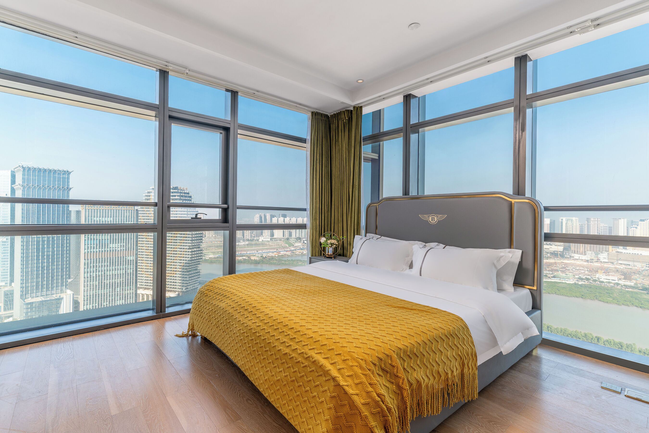 A large bedroom with a bed, a view of the city, and a window with a curtain.