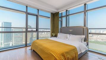 A large bedroom with a bed, a view of the city, and a window with a curtain.