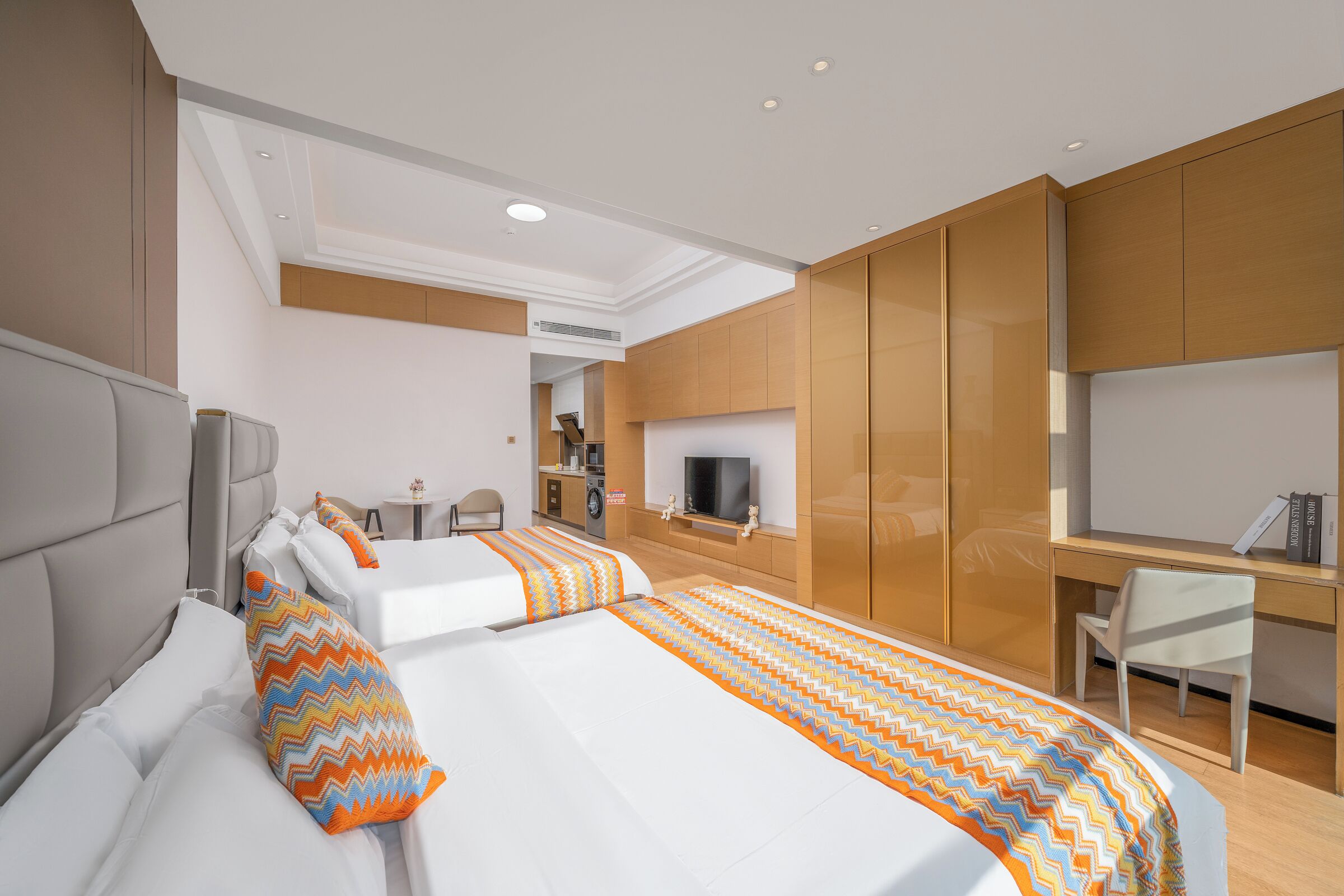 A hotel room with two beds, a desk, a television, and a kitchenette.