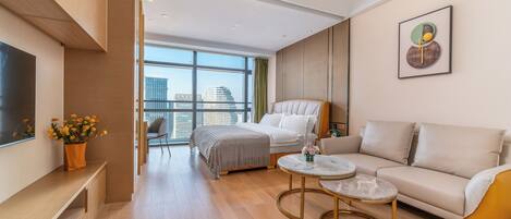 Quarto de hotel moderno com cama, sofá, mesa de centro e uma grande janela com vista para a cidade.