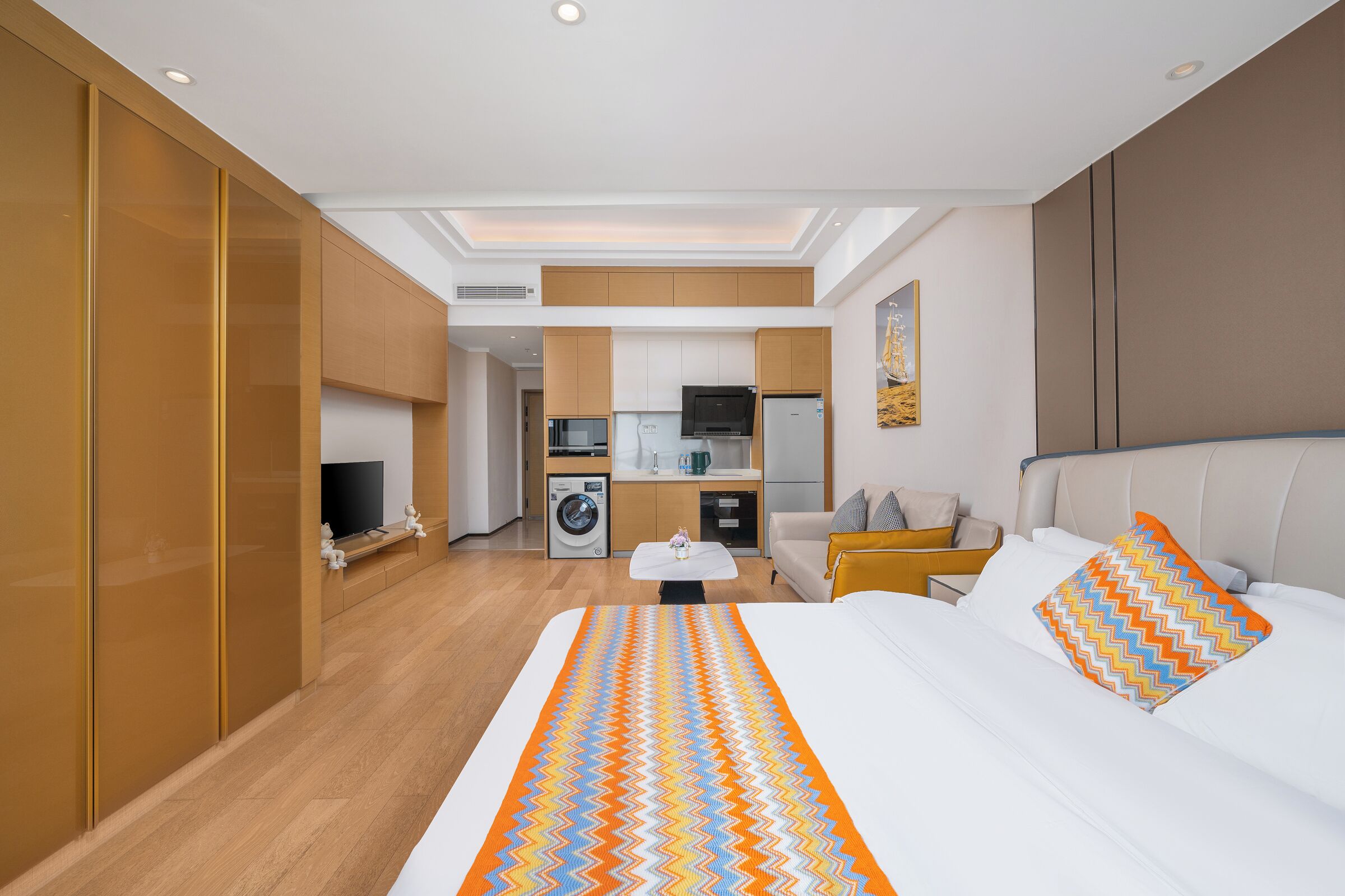 A hotel room with a bed, a TV, a kitchenette, and a bathroom.