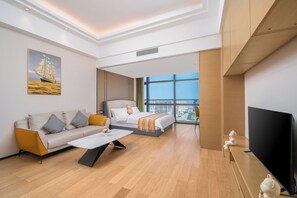 A modern hotel room with a sofa, a bed, a flat-screen TV, and a large window offering a city view.