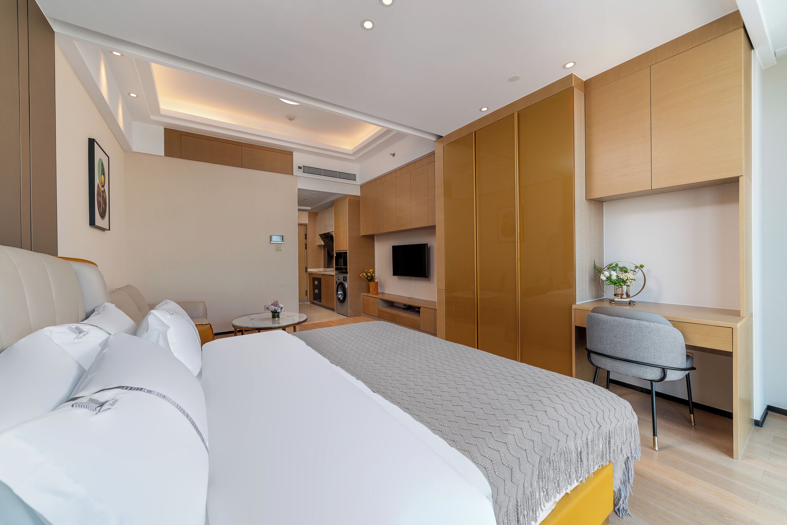 A hotel room with a bed, a desk, a chair, a TV, and a kitchenette.