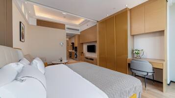 A hotel room with a bed, a desk, a chair, a TV, and a kitchenette.