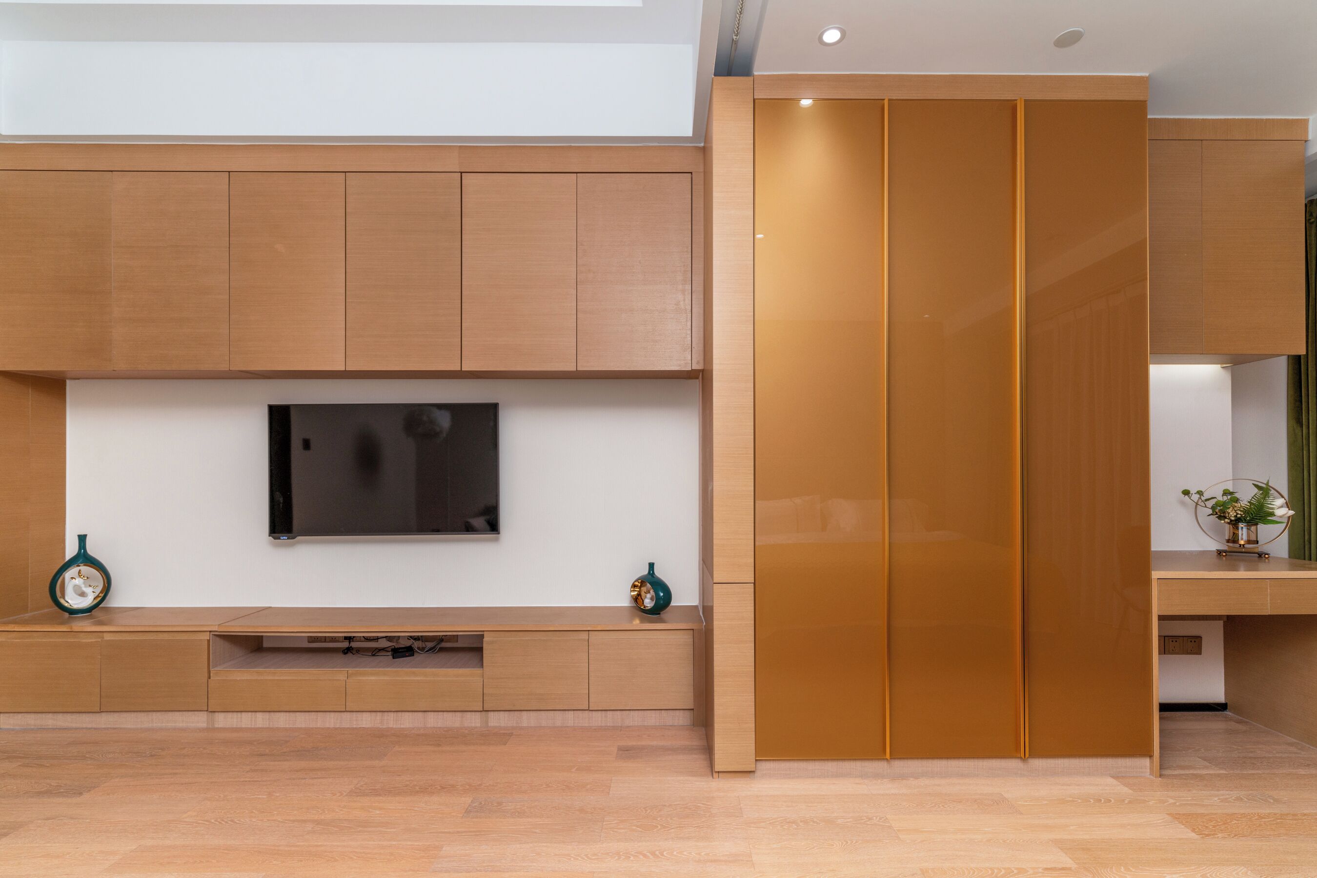 A modern interior with a flat-screen TV mounted on a wall, wooden cabinetry, and a sliding door.