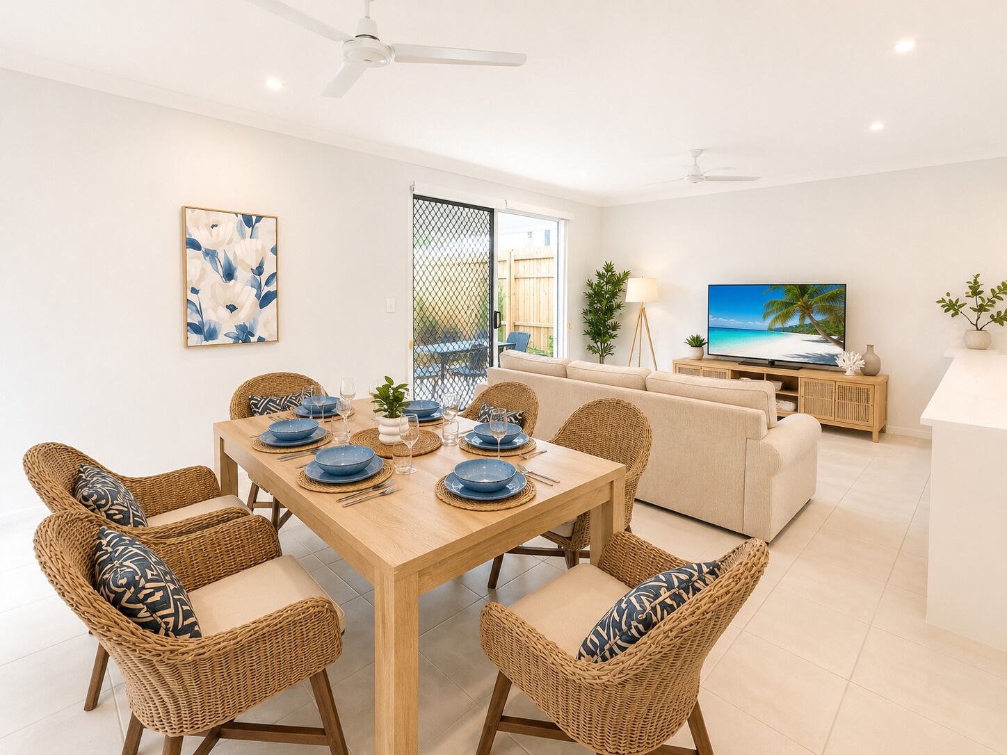 A dining area with a wooden table set for four, surrounded by wicker chairs with cushions.
