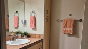 Een badkamer met wastafel, spiegel, handdoekhouder en een douchehoek.