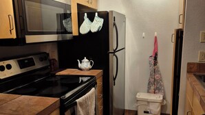 Een kleine keuken met houten kastjes, een magnetron, een kookplaat, een koelkast en een badkamer met een toilet en een prullenbak.