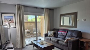 Een woonkamer met een bank, salontafel, televisie en een schuifdeur die uitkomt op een terras.