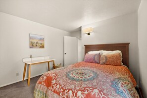 Une chambre à coucher avec un lit, une table de chevet, une lampe fixée au mur et un tableau accroché au mur.