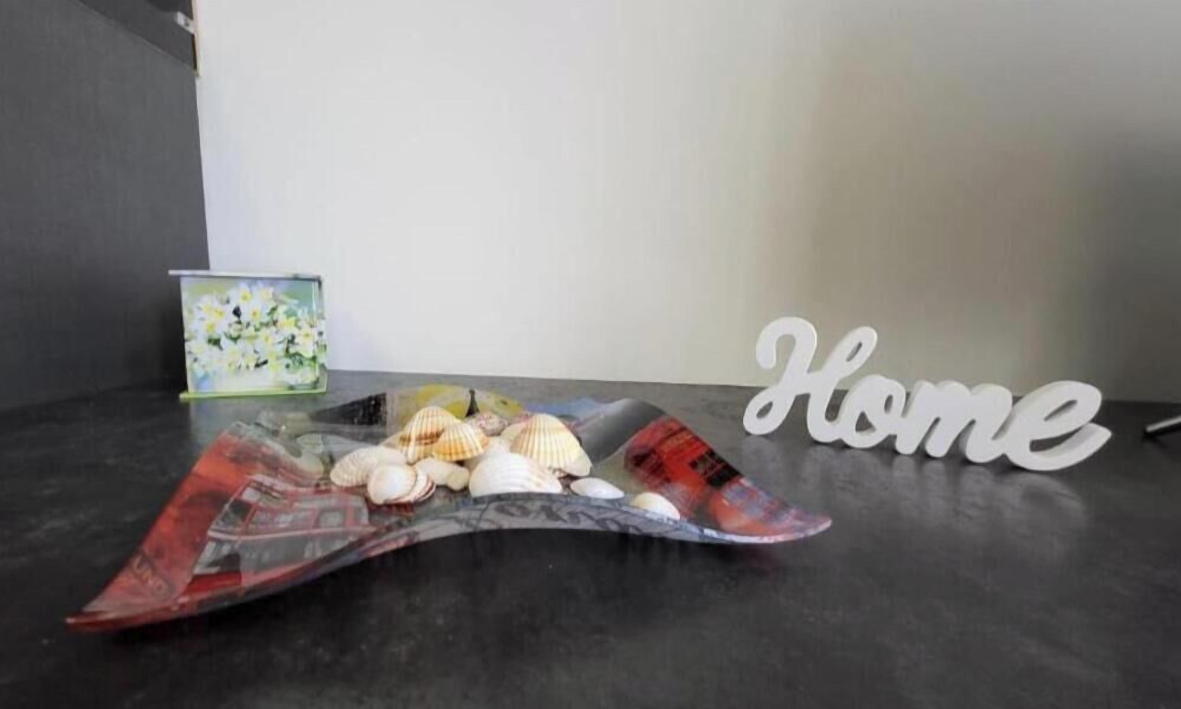 Een tafel met schelpen, een boek, een naambordje met 'Home' erop en een ingelijst foto op een donker oppervlak.