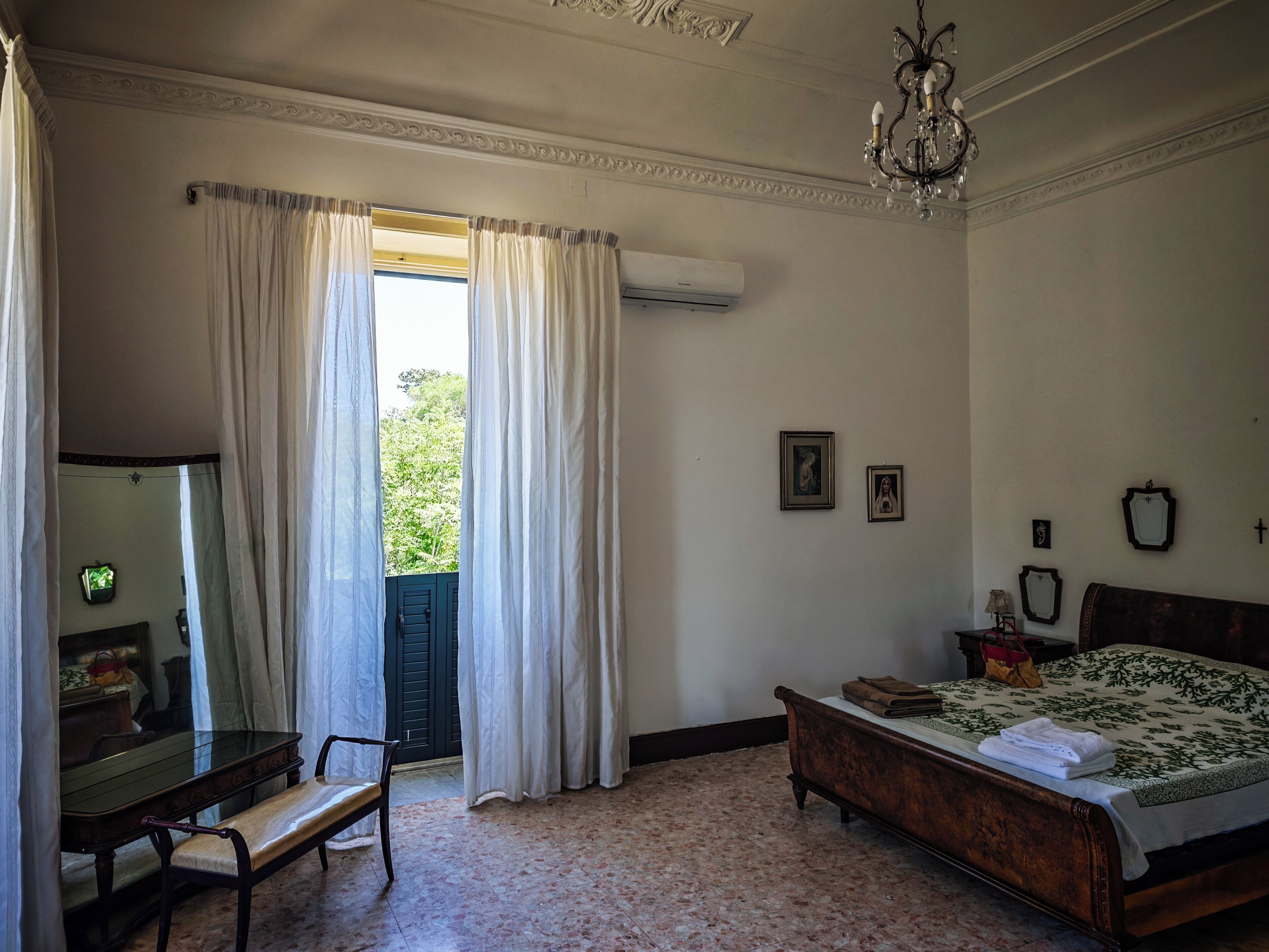Un dormitorio con cama, banco, espejo y candelabro.