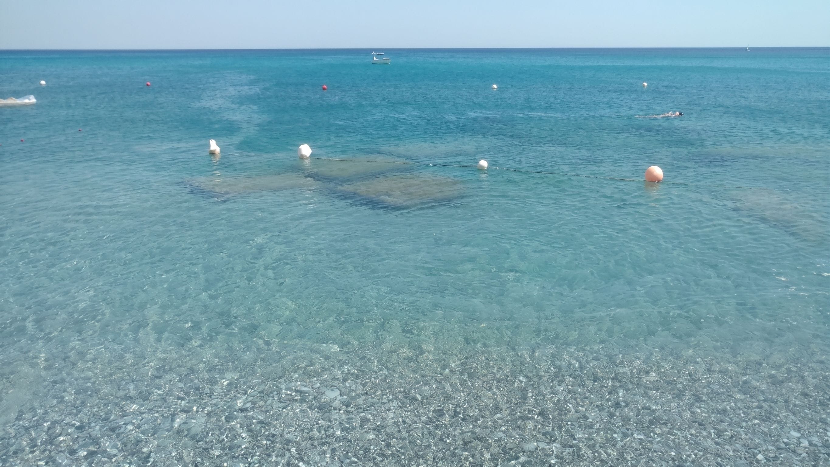 A clear view of a beach with shallow water, pebbles, and buoys.