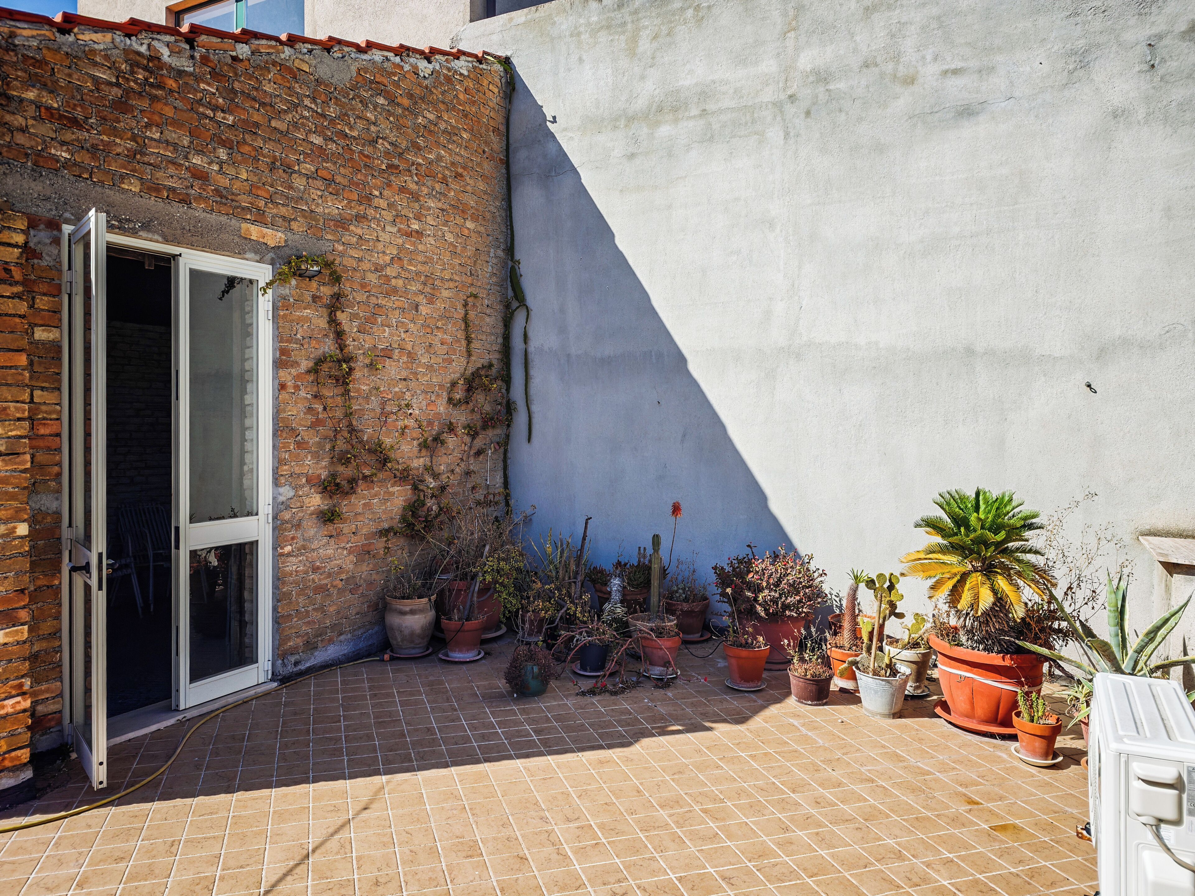 Un patio con plantas en macetas, una puerta corrediza de vidrio y un muro de ladrillo.