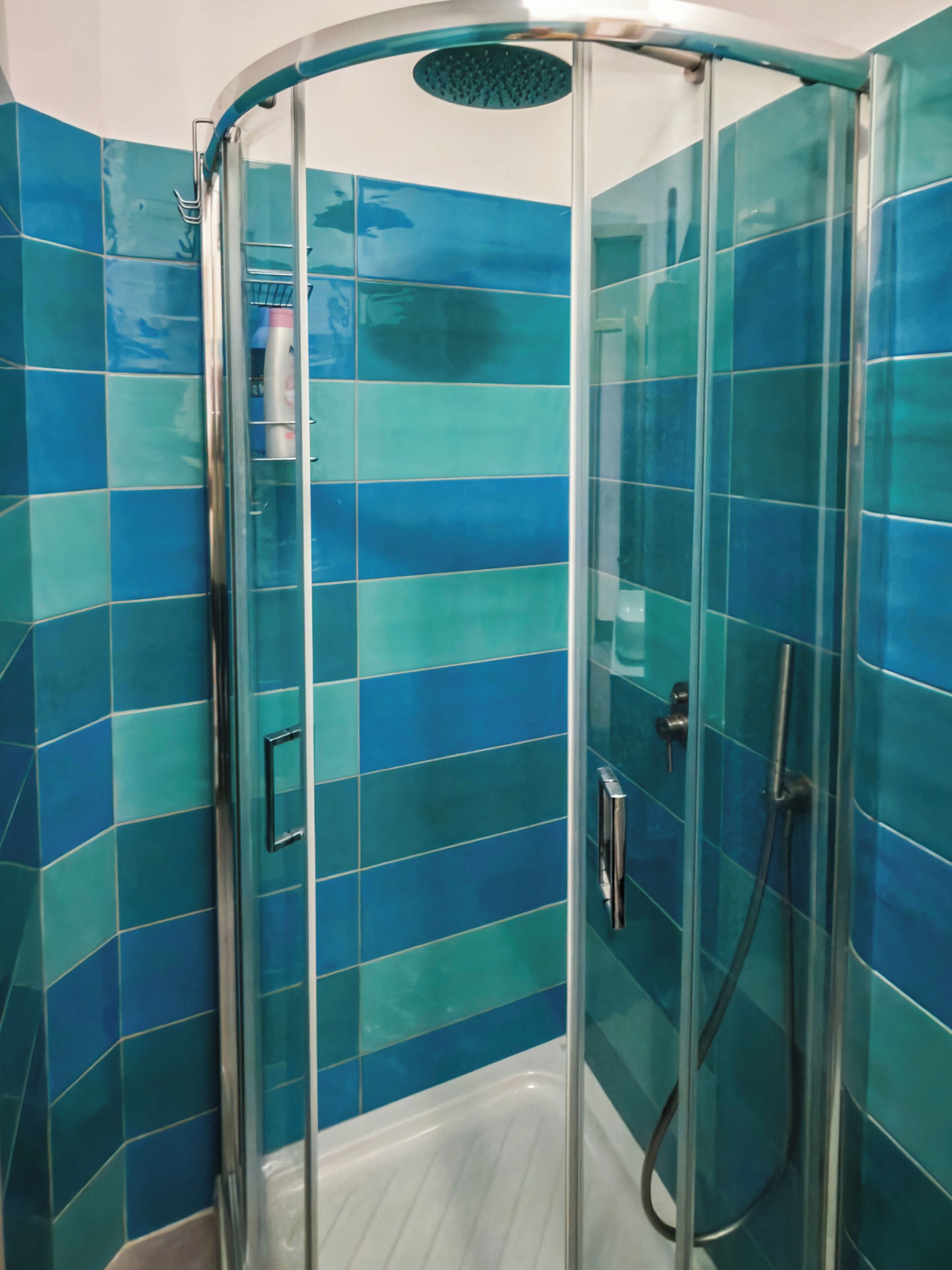 Una cabina doccia in vetro con pareti piastrellate di blu e pavimento bianco.