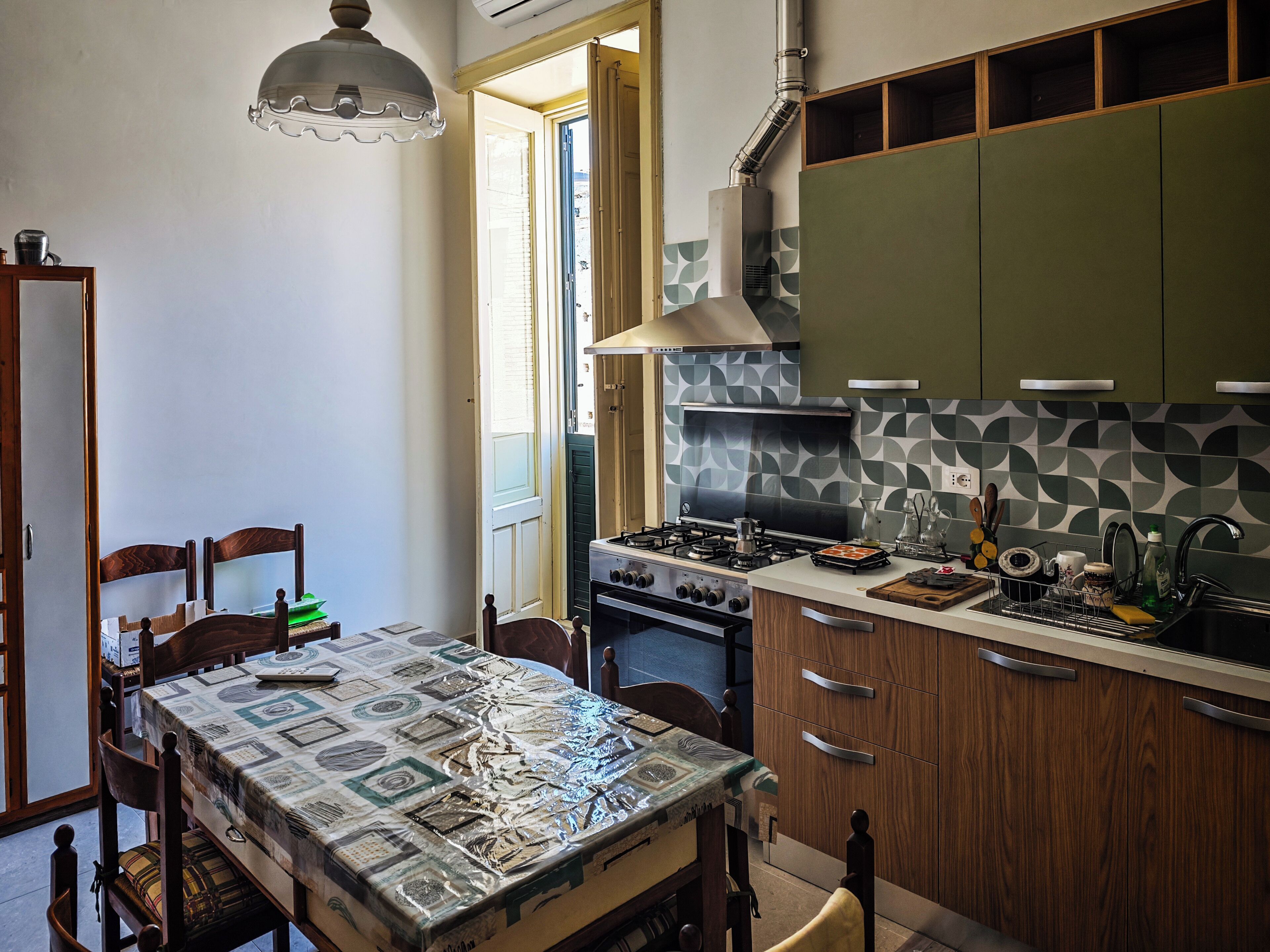 A kitchen with a stove, oven, and green cabinets. There is a dining table with chairs and a patterned tablecloth.