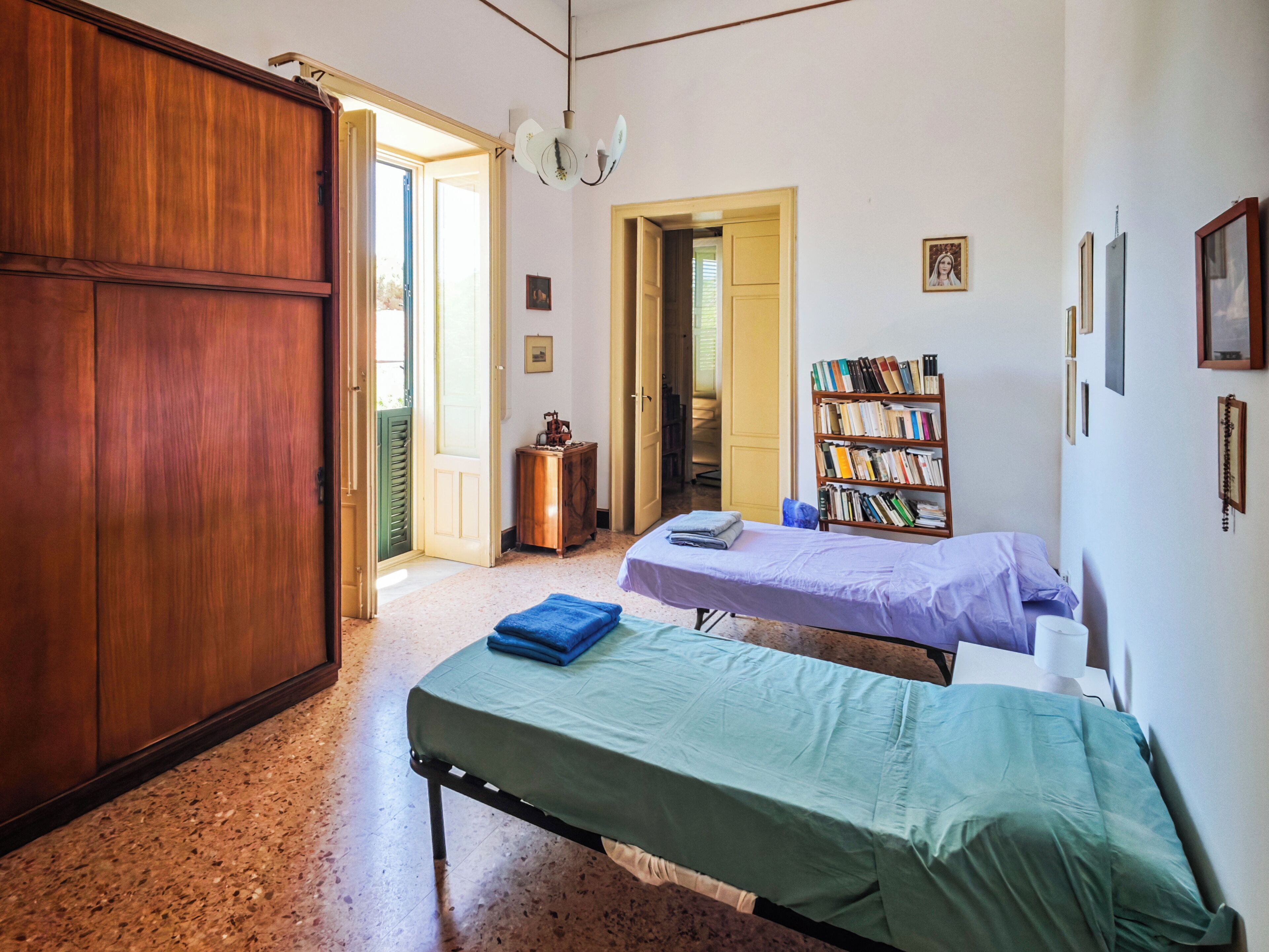 A room with a bed, a bookshelf, a wardrobe, and a door leading to another room.