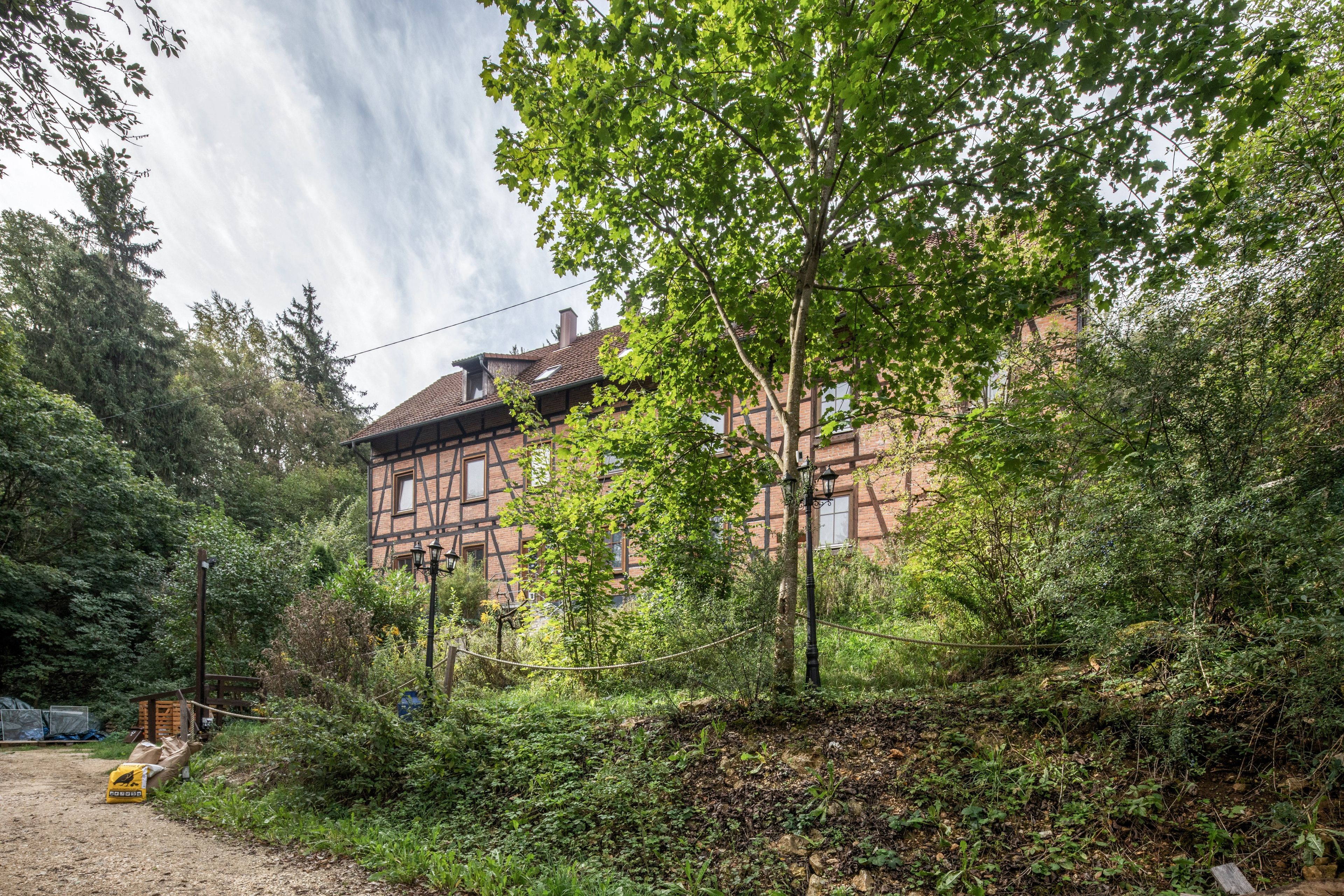 A traditional half-timbered house surrounded by dense greenery and a dirt path.