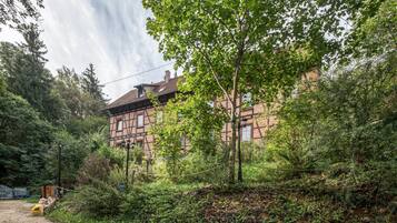 A traditional half-timbered house surrounded by dense greenery and a dirt path.