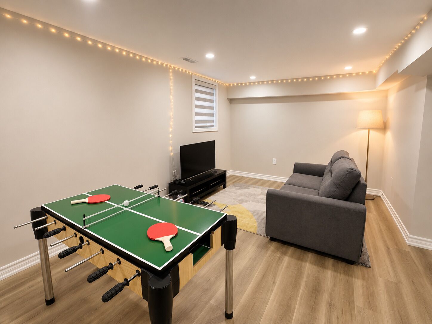 Una habitación con mesa de ping pong, sofá, televisión y lámpara.
