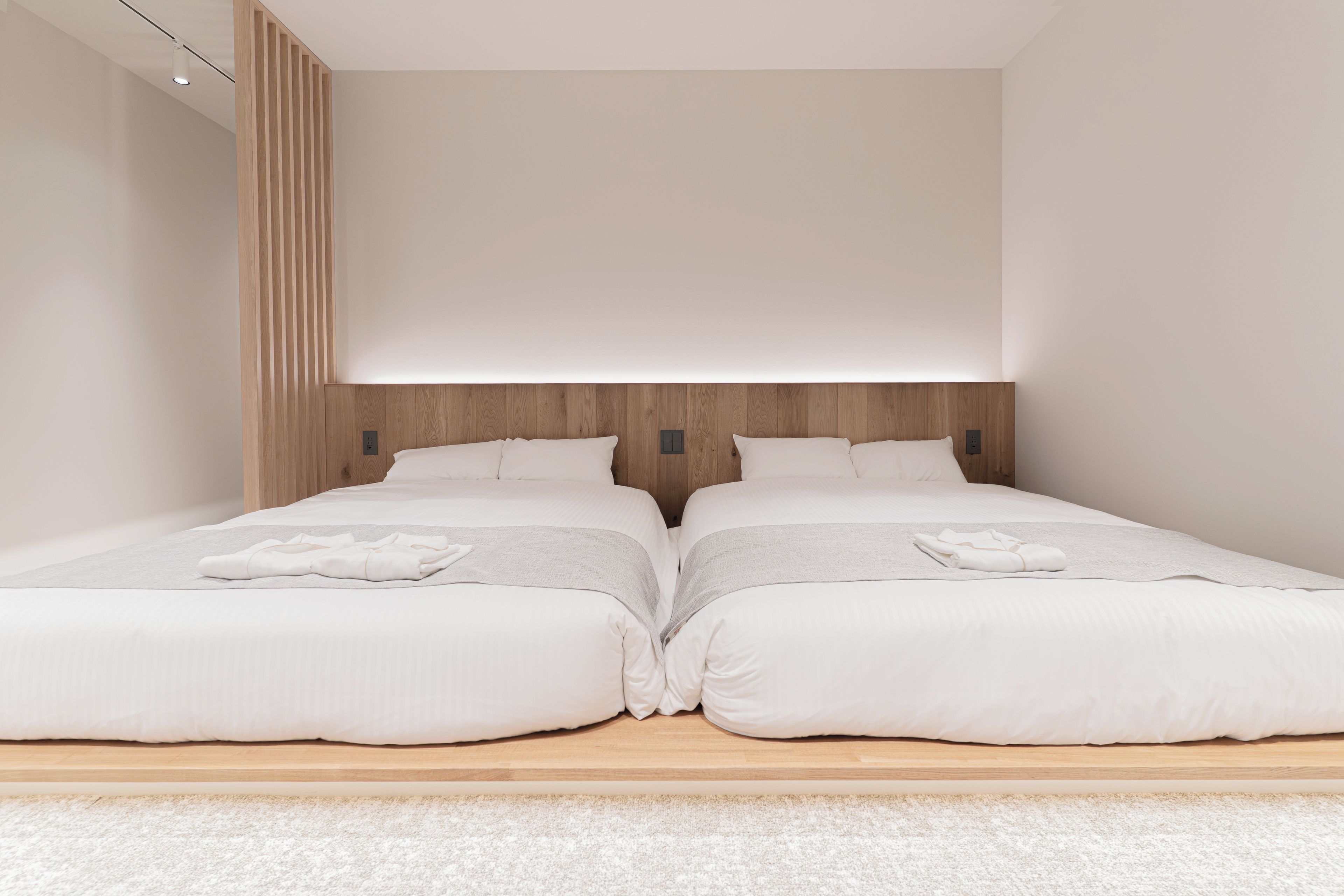 Ein modernes Schlafzimmer mit zwei Betten, einem Holzkopfstück und einer neutralen Farbgestaltung.