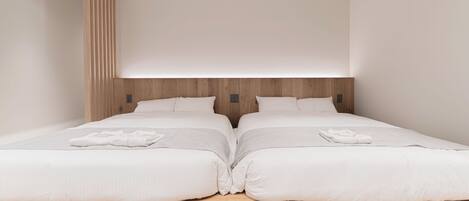 Ein modernes Schlafzimmer mit zwei Betten, einem Holzkopfstück und einer neutralen Farbgestaltung.