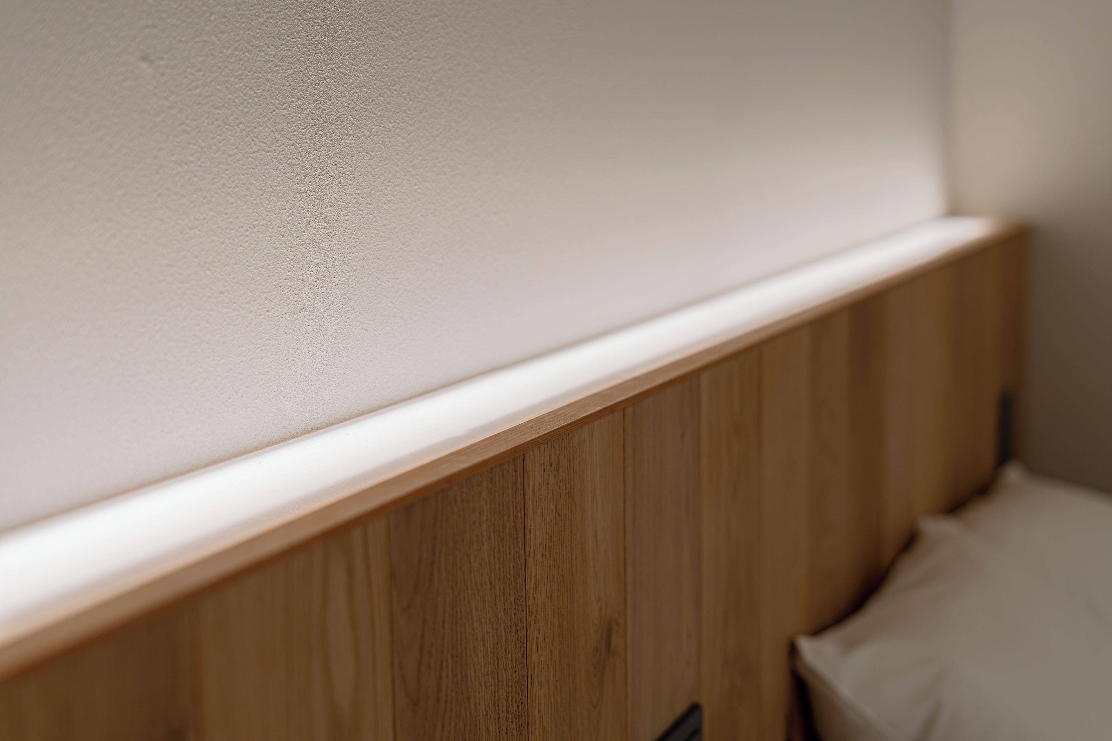 A close-up of a wooden headboard with a white trim against a textured wall.