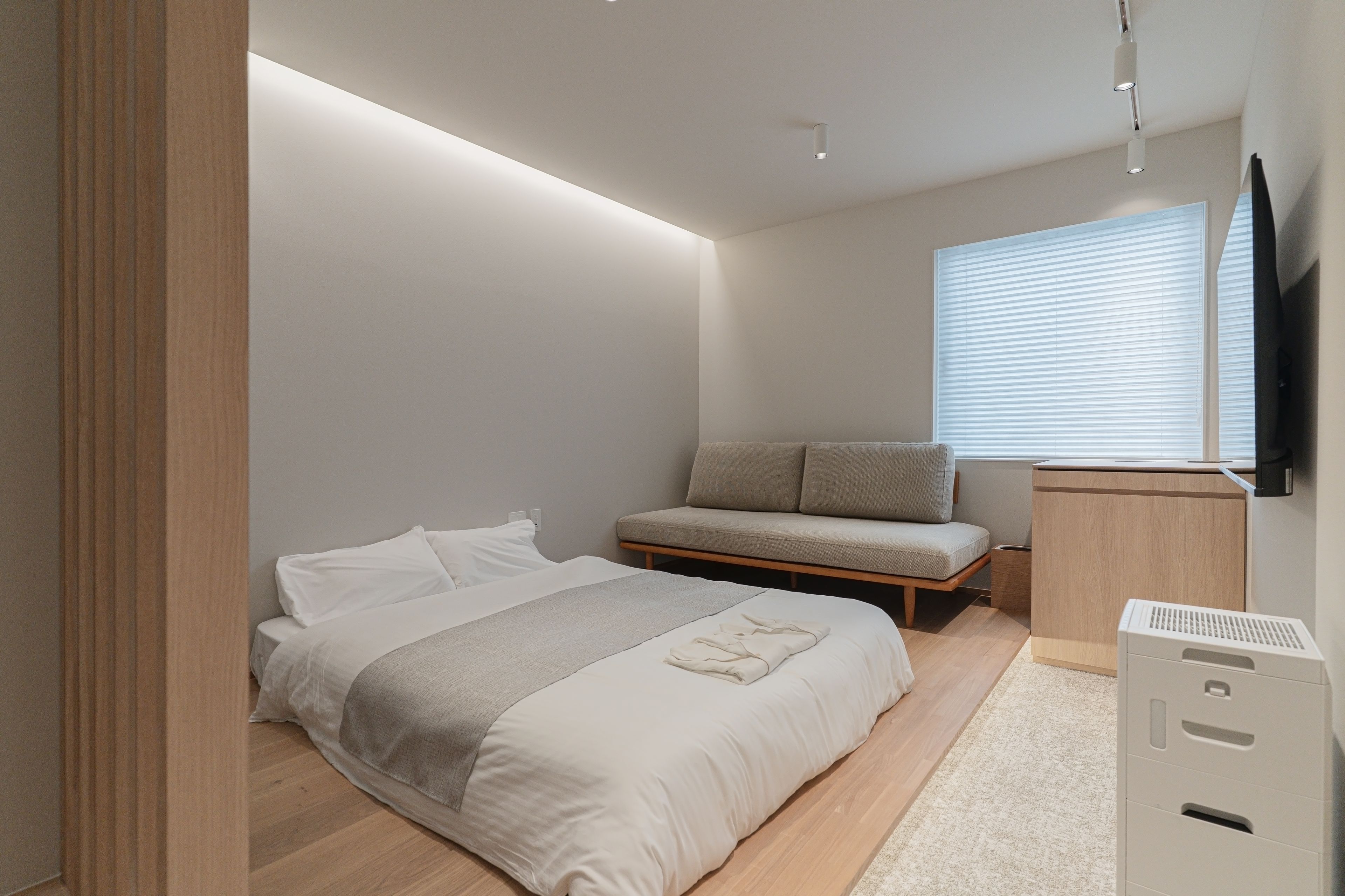 Une chambre à coucher avec un lit, un canapé, une télévision et une fenêtre avec des stores.