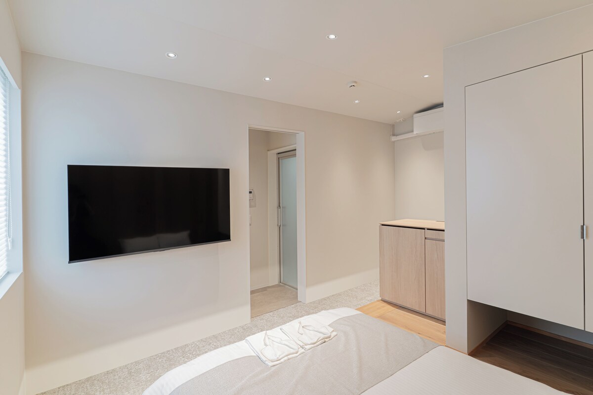 A modern bedroom with a flat-screen TV mounted on the wall, a bed with a white comforter, and a wooden cabinet.