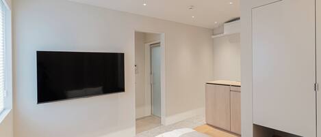 Un dormitorio moderno con una televisión de pantalla plana montada en la pared, una cama con edredón blanco y un armario de madera.