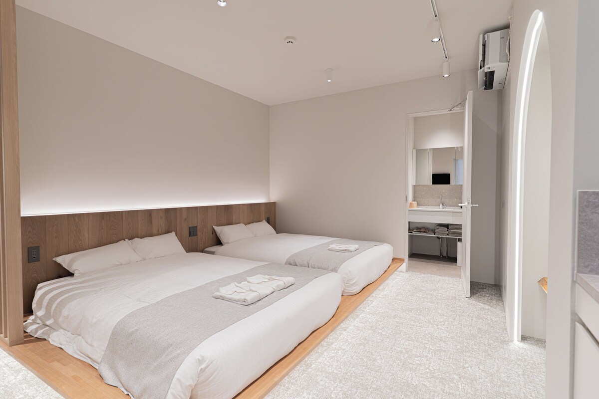 A modern bedroom with two beds, a built-in wardrobe, and a bathroom with a mirror.