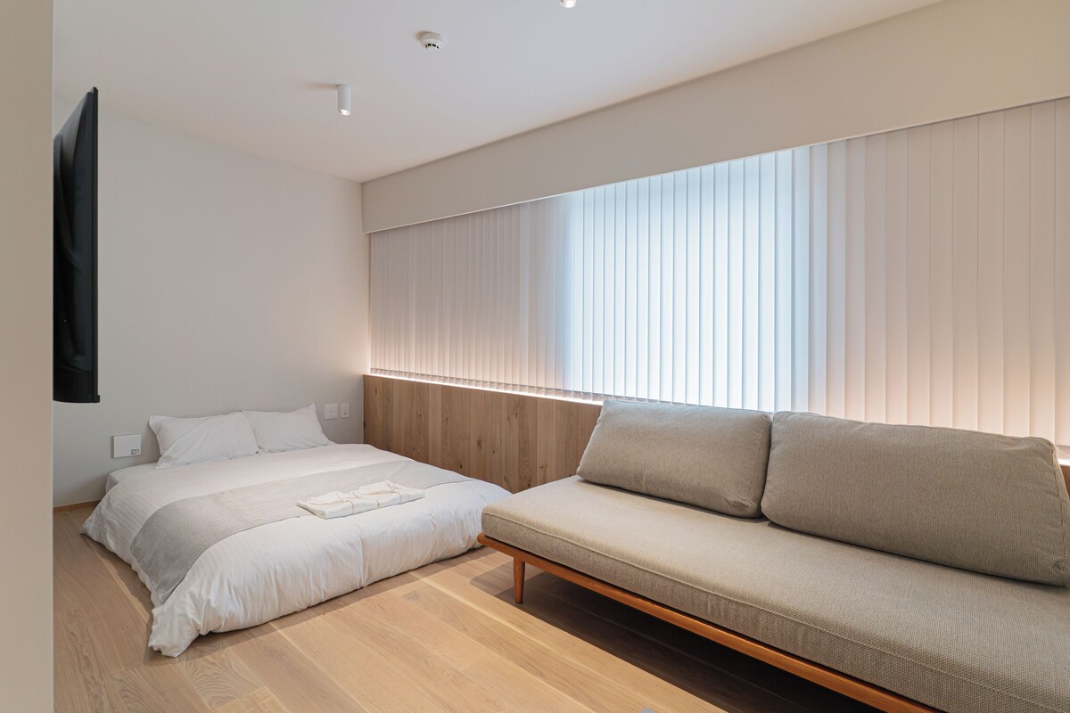 Un dormitorio moderno con una cama, un sofá y un amplio ventanal con persianas.