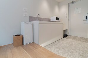 A compact kitchenette with a refrigerator, microwave, and a small trash bin. - Giraffe Nakasu haku (Fukuoka)