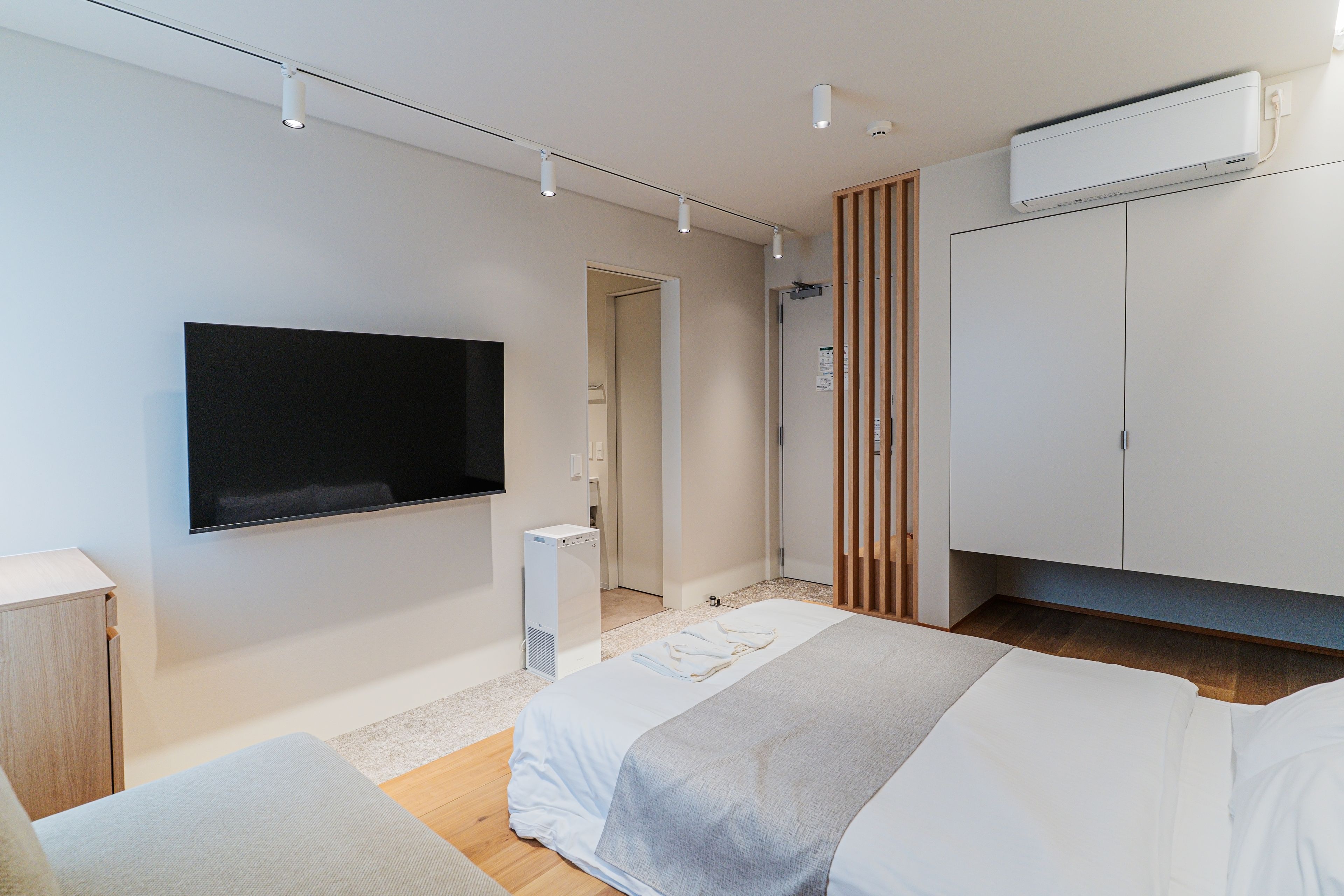 A modern bedroom with a bed, a TV mounted on the wall, and a wardrobe.