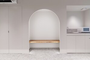 A minimalist room with a wooden bench, a microwave, and a cabinet. - Giraffe Nakasu haku (Fukuoka)