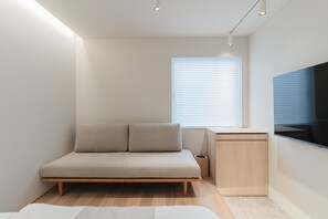 A modern bedroom with a minimalist design, featuring a bed, a sofa, a TV, and a small desk. - Giraffe Nakasu haku (Fukuoka)