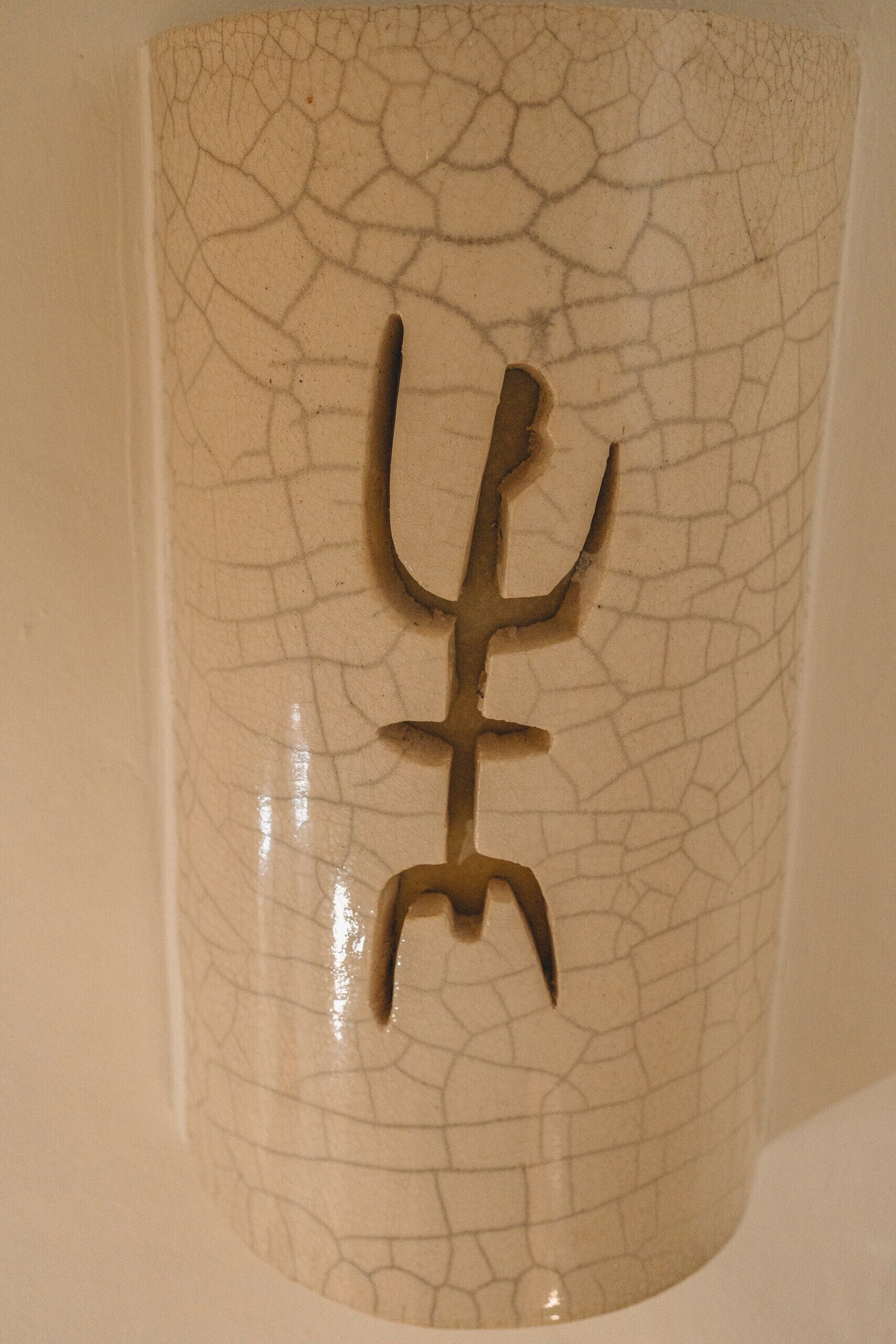 En keramisk mugg med en strukturerad yta och en symbol bestående av tre sammanlänkade element.
