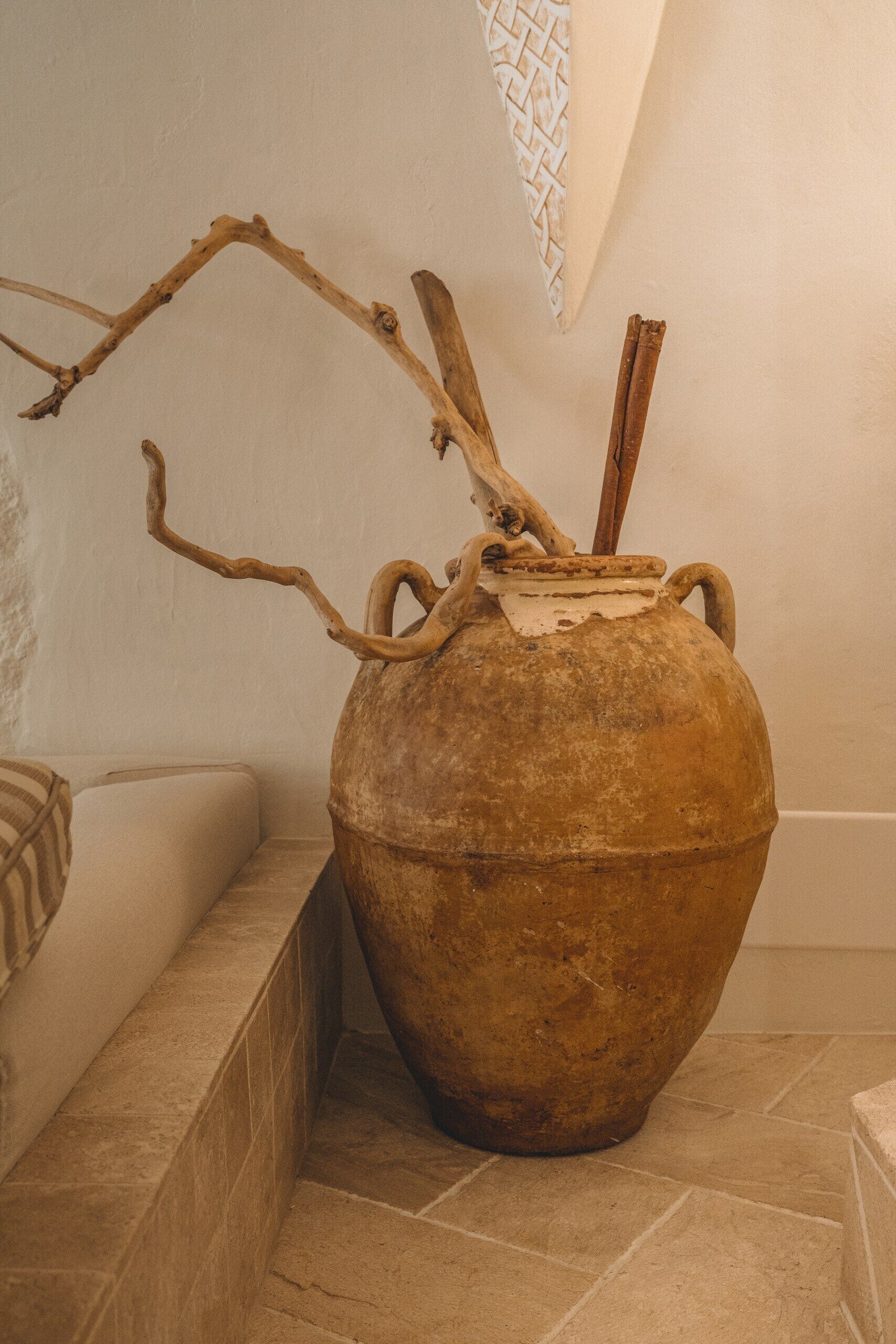 A large ceramic pot with a branch and cinnamon sticks on a tiled floor.