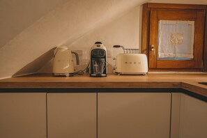 Una cocina con armarios blancos, cafetera, tostadora y una puerta con panel decorativo.