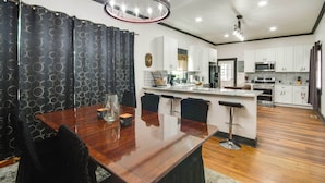 A modern kitchen with white cabinets, a central island, and a dining area with a wooden table and black chairs. - Family-Friendly Retreat w/ Fireplaces in Greenwood (Greenwood)