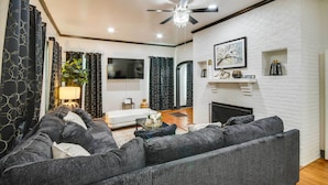 A modern living room with a fireplace, dark grey sofas, a ceiling fan, and a TV mounted on the wall. - Family-Friendly Retreat w/ Fireplaces in Greenwood (Greenwood)