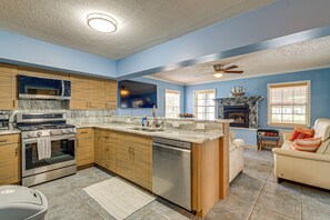 A kitchen with a stove, oven, and dishwasher, a dining area with a table and chairs, and a living room with a sofa and fireplace. - Scallop HQ: 3 Boat Docks and Free Golf Cart! (Homosassa)